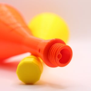 May include: Two plastic party noisemakers, one orange and one yellow, with a close-up of the orange noisemaker's mouthpiece.