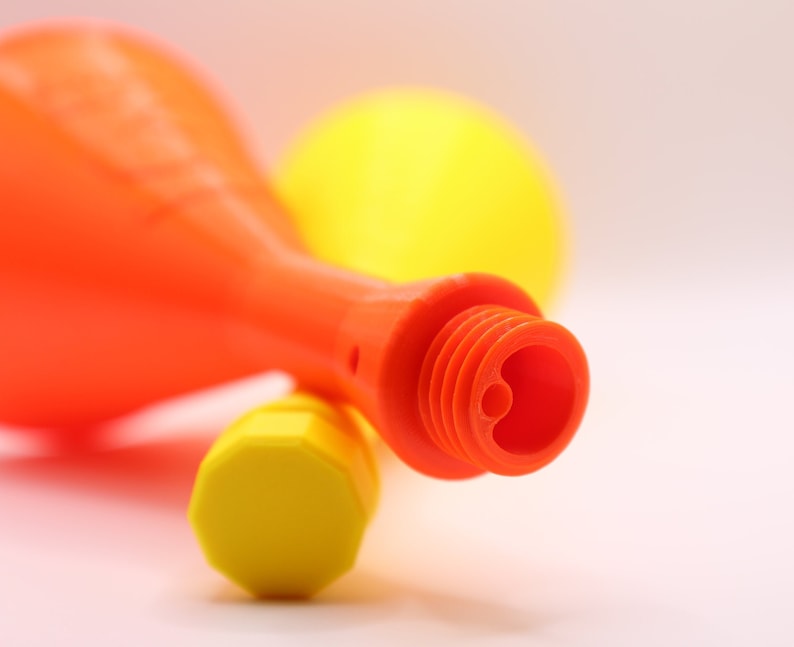 May include: Two plastic party noisemakers, one orange and one yellow, with a close-up of the orange noisemaker's mouthpiece.