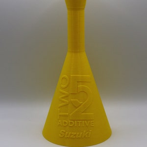 May include: A yellow plastic bottle with a narrow neck and a wide base. The bottle is labeled "TWO 52 ADDITIVE Suzuki".