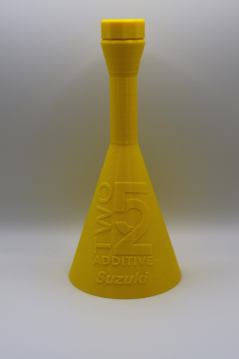 May include: A yellow plastic bottle with a narrow neck and a wide base. The bottle is labeled "TWO 52 ADDITIVE Suzuki".