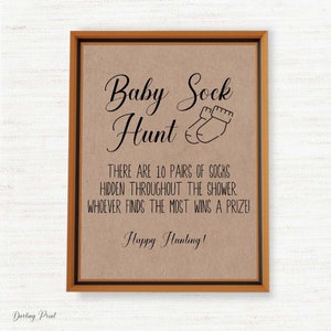 May include: A brown paper sign with a brown wooden frame. The sign says "Baby Sock Hunt" with a drawing of two baby socks. The text below says "There are 10 pairs of socks hidden throughout the shower. Whoever finds the most wins a prize! Happy Hunting!"