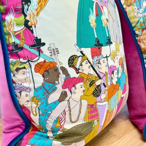 May include: A colorful throw pillow with a white background and a pattern of people playing musical instruments. The pillow has a pink and teal border.