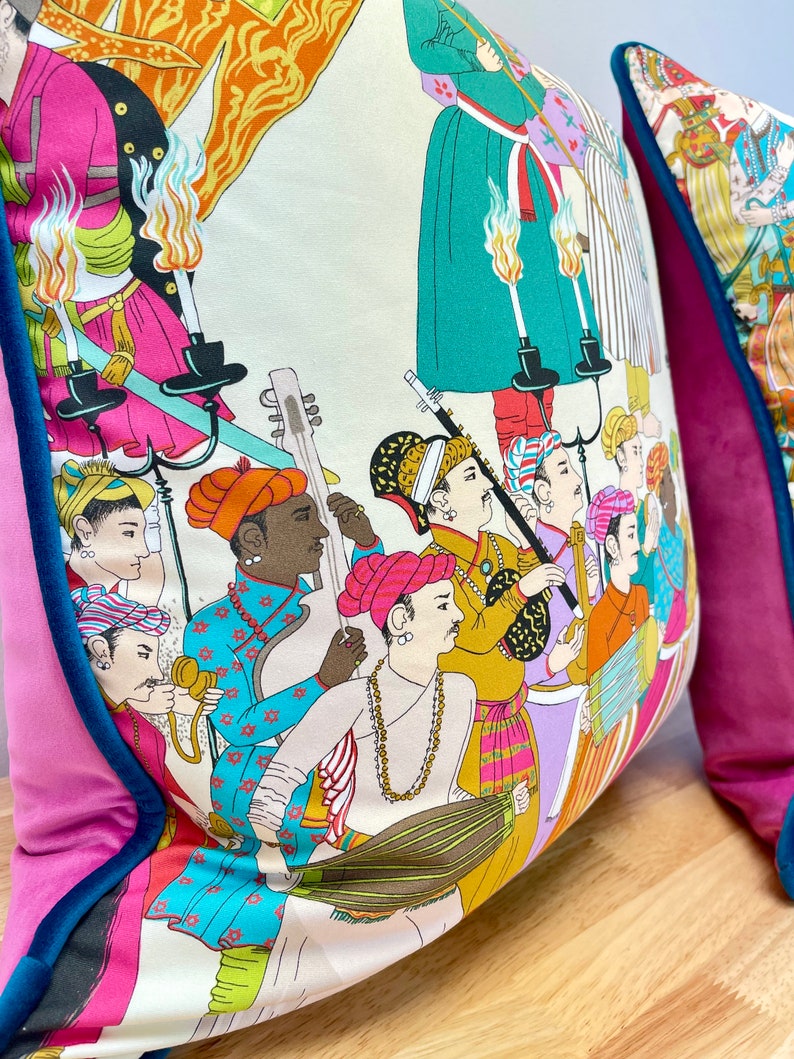 May include: A colorful throw pillow with a white background and a pattern of people playing musical instruments. The pillow has a pink and teal border.