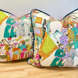 May include: Two decorative throw pillows with a white background and colorful illustrations of people and animals. The pillows have a teal blue trim.