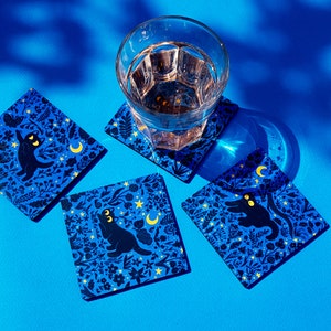May include: Four blue coasters with a black cat and moon design. The coasters are made of a durable material and are perfect for protecting your furniture from spills and scratches.