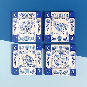 Può includere: Set di quattro sottobicchieri in ceramica blu e bianca con un design a gatto. Ogni sottobicchiere presenta una posa di gatto diversa e un motivo floreale.