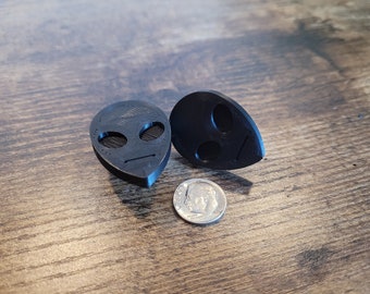 May include: Two black alien face shaped guitar picks. The picks are about the size of a dime.