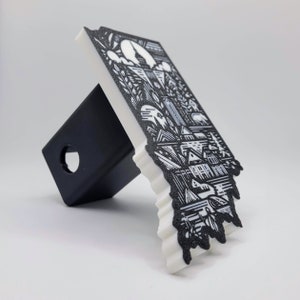 May include: White and black hitch cover with a detailed illustration of a city skyline. The design features buildings, trees, and other city elements.