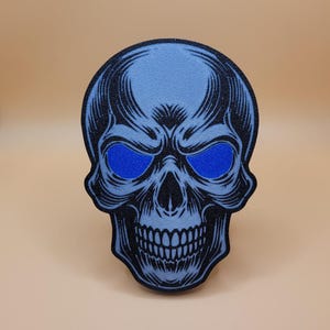 May include: A blue skull with black outlines and blue eyes. The skull has a detailed design with a menacing expression.