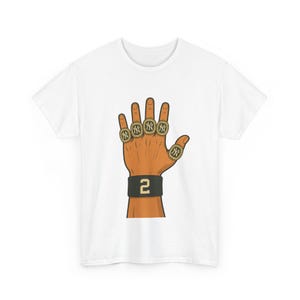 May include: White t-shirt featuring a cartoon illustration of a hand wearing five championship rings. The rings are gold with the New York Yankees logo. A black wristband displays the number "2".