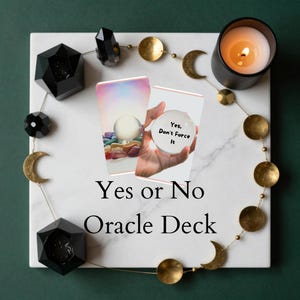 May include: A white marble surface with a Yes or No Oracle Deck. The image includes a lit candle, crystals, and cards with a crystal ball. The text on one card reads "Yes, Don't Force It."