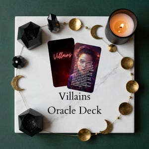 May include: An oracle deck titled "Villains" with two cards featuring text and a portrait. The deck is on a white marble surface, surrounded by decorative elements including a lit candle, black geometric shapes, and gold-colored moons and circles.