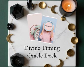 May include: A styled image featuring a Divine Timing Oracle Deck. The image includes a lit candle, decorative crystals, and a gold moon and circle garland. Two cards are visible, one with a clock and the other with the word "December".