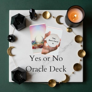 May include: A white marble surface with a Yes or No Oracle Deck. The image includes a lit candle, crystals, and cards with a crystal ball. The text on one card reads "Yes, Don't Force It."
