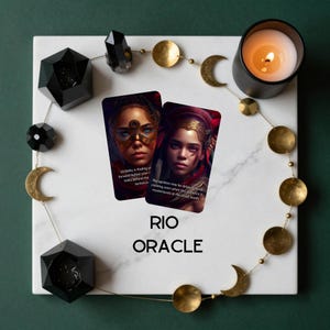 May include: Two rectangular oracle cards featuring portraits of individuals in ornate headgear, labelled RIO ORACLE. The cards are arranged on a white marble square surrounded by a gold-toned moon phase garland, black geometric crystals, and a lit candle.