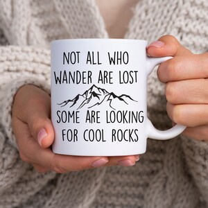 May include: White ceramic mug with a black mountain range graphic and the text "Not all who wander are lost, some are looking for cool rocks".