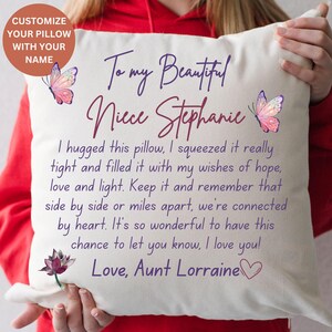 May include: Cream cushion with a personalized message to "Niece Stephanie" from "Aunt Lorraine." The cushion features butterfly and lotus flower illustrations. Text includes "Customize Your Pillow With Your Name."