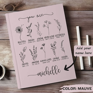 May include: A mauve journal with a floral design and the text "you are" at the top. The journal has a list of positive affirmations with bible verses. The text "michelle" is written at the bottom of the journal. The text "Add your name here" is written in a white box on the right side of the journal. The text "COLOR: MAUVE" is written at the bottom of the journal.