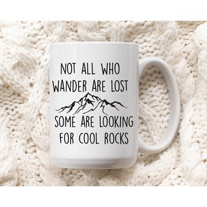 May include: White ceramic mug with a black mountain range graphic and the text "Not all who wander are lost, some are looking for cool rocks."