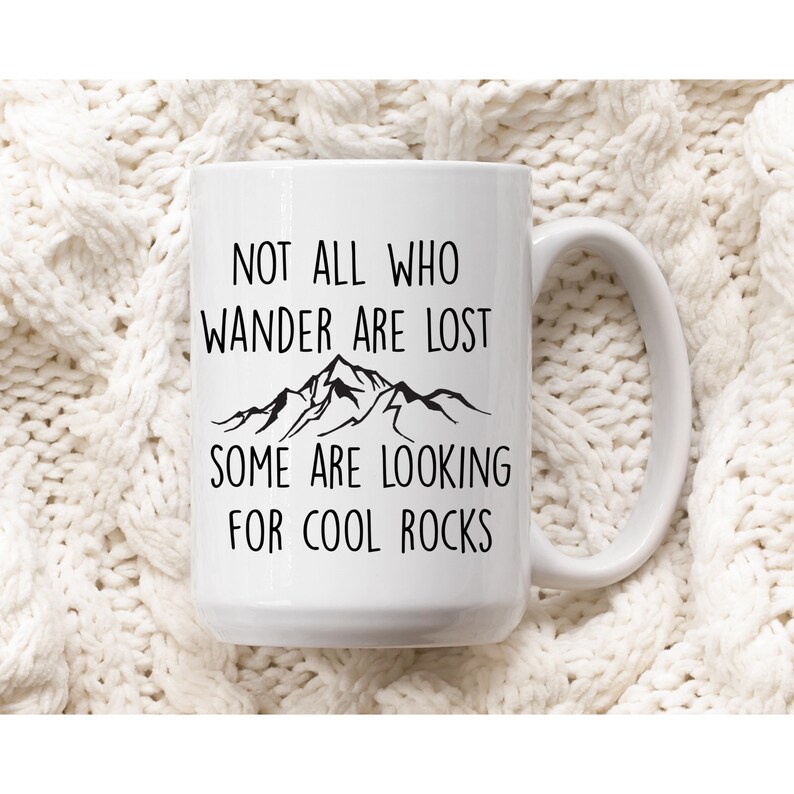 May include: White ceramic mug with a black mountain range graphic and the text "Not all who wander are lost, some are looking for cool rocks."