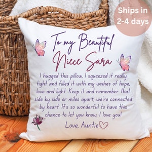 May include: White square cushion with text, butterflies, and a lotus flower. The cushion reads "To my Beautiful Niece Sara" and includes a heartfelt message from "Love, Auntie". The cushion is placed near a woven basket.