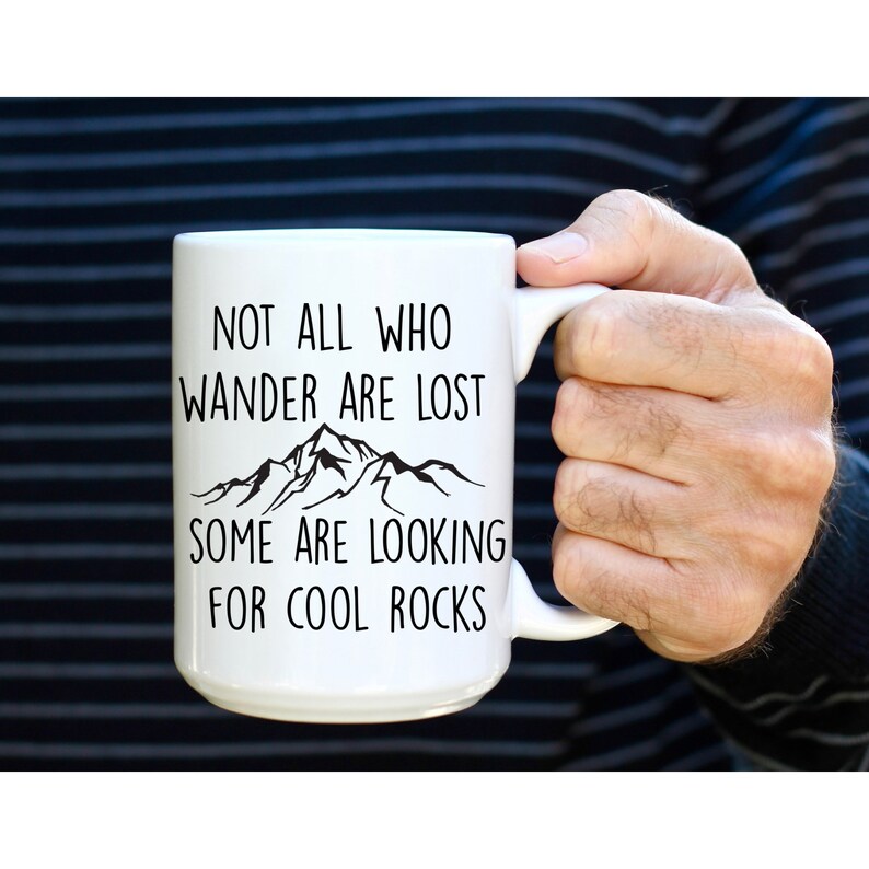 May include: White ceramic mug with a black mountain range graphic and the text "Not all who wander are lost, some are looking for cool rocks."
