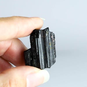 May include: A black tourmaline crystal with striations and a rough, natural texture.