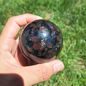 May include: A black sphere with red and gold flecks. The sphere is made of polished stone and has a smooth, shiny surface.