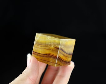 May include: A yellow and brown fluorite cube with striations. The cube is about 2 inches in size.