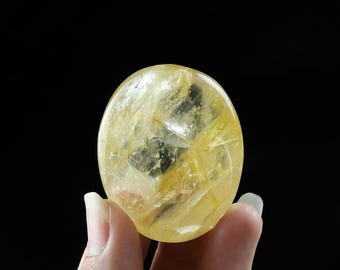 Puede incluir: Una esfera de cristal de citrino amarillo lisa con un patrón translúcido en espiral. La esfera está siendo sostenida en una mano.