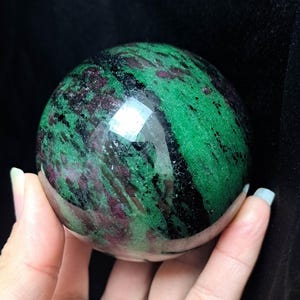 Könnte beinhalten: Eine polierte Zoisit-Kugel, eine Art Edelstein, in Grün, Schwarz und Rosa.