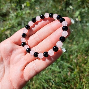 May include: A bracelet made of black and pink beads. The bracelet is made of alternating black and pink beads.