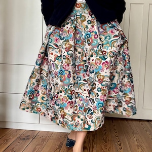 Peut inclure: Jupe colorée à motifs avec un motif floral tourbillonnant dans les tons de bleu, rose, vert et marron. La jupe est associée à une veste bleu marine et des ballerines bleues. Le tissu de la jupe a un fond crème.