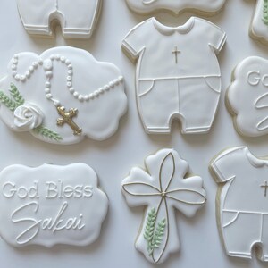 Pode incluir: Biscoitos de a&ccedil;&uacute;car branco decorados com glac&ecirc; real. Os biscoitos apresentam uma cruz, um ros&aacute;rio, um macac&atilde;o de beb&ecirc; e o texto "God Bless Sakai".