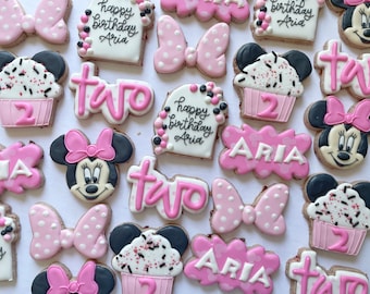 May include: A collection of pink and black decorated sugar cookies featuring a cupcake, a bow, the word "two", and a cartoon mouse with a bow. The cookies are decorated with pink, black, and white icing and sprinkles. The cookies say "Happy Birthday Aria" and "Aria" on some of the cookies.