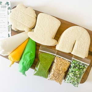 May include: A St. Patrick's Day cookie decorating kit with cookie shapes, icing bags, and sprinkles. The kit includes a shamrock, top hat, and horseshoe-shaped cookies, along with green, yellow, and white icing.