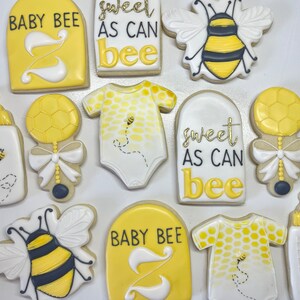 K&ouml;nnte beinhalten: Ein Set aus neun gelben und wei&szlig;en, verzierten Zuckerkeksen mit Bienen- und Babymotiven. Die Kekse zeigen Bilder von Bienen, Babyflaschen, Stramplern und den Text "Baby Bee" und "Sweet as can bee".