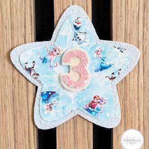 May include: A star-shaped craft featuring characters from the film Frozen, with a light blue background and the number 3 in pink. The design includes images of Elsa, Anna, and Olaf, with a white glittery border.