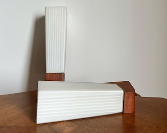 Op de afbeelding: Twee witte keramische tafellampen met een houten voet. De lampen hebben een geribbelde textuur en staan op een houten oppervlak.