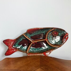 Peut inclure: Un plat de service en céramique en forme de poisson avec quatre compartiments. Le plat est décoré d'un glaçage vert, brun et rouge.