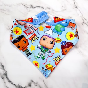 Op de afbeelding: Lichtblauwe baby slabbetje met een Toy Story print. Het slabbetje heeft een drukknoopsluiting en is versierd met figuren als Buzz Lightyear en Woody. Gemaakt van zachte stof.