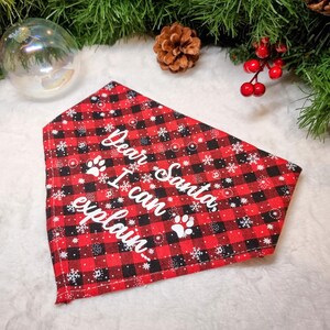 May include: Red and black plaid dog bandana with white text that reads "Dear Santa, I can explain." The bandana has white paw prints and snowflake accents. The bandana is a holiday-themed pet accessory.