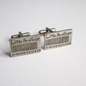 May include: A pair of silver cufflinks with the words "Little Brother" and a barcode with the date "21-18-20-8-5-2-5-19-20" engraved on them.