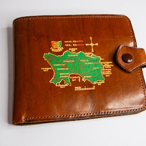 May include: A brown leather wallet with a map of Jersey, a British island, printed on the front. The map is in green and gold, with the island's name and various locations labeled.
