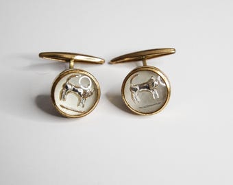 May include: A pair of gold cufflinks with a white background and a silver bull design.
