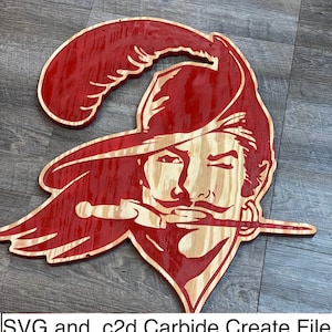 Puede incluir: Un recorte de madera rojo de un pirata con un sombrero de plumas y una espada. El pirata lleva un sombrero rojo con una pluma y tiene bigote y barba. El pirata mira hacia la derecha.