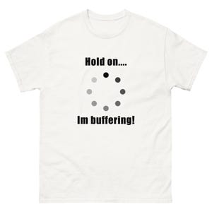 May include: White t-shirt featuring the text "Hold on.... Im buffering!" in black. The design includes a circular loading symbol with black and grey dots, a humorous reference to internet loading.