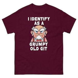 Può includere: T-shirt bordeaux con la scritta bianca "I IDENTIFY AS A GRUMPY OLD GIT". La maglietta presenta un'illustrazione a cartoni animati di un vecchio brontolone con barba e sopracciglia bianche, con un papillon rosso.