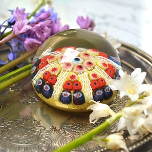May include: A glass paperweight with a colorful, multi-layered design of red, white, and blue flowers. The paperweight is sitting on a silver tray with a floral design.