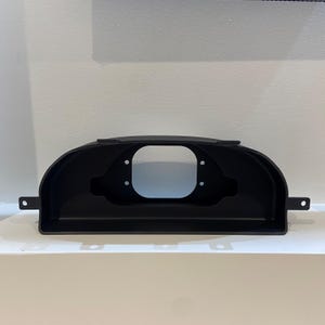 May include: Black plastic gauge pod with four holes for mounting gauges. The pod is curved to fit a car's dashboard.